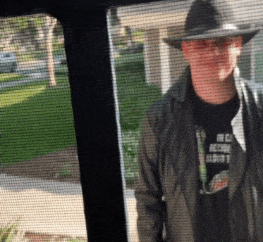 a man wearing a hat and a shirt that says mc on it stands in front of a screen door
