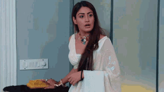 a woman wearing a white saree and a necklace is standing in a bedroom
