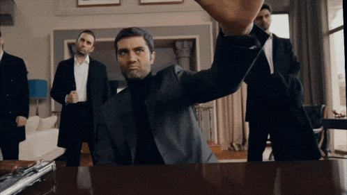 a man in a suit is sitting at a table with a gun on it