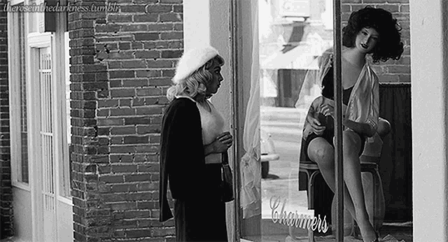 a black and white photo of two women standing in front of a store window .