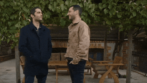 two men standing next to each other in front of a building