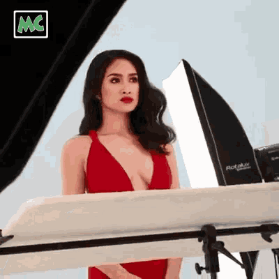 a woman in a red bikini is standing in front of a camera and a light .