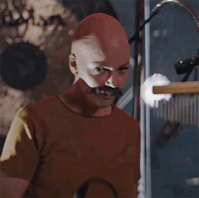 a bald man with a mustache is standing in front of a microphone ..