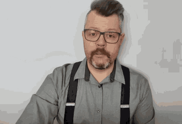 a man with glasses and suspenders looks surprised