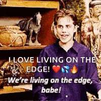 a man in a purple shirt is standing in front of a shelf with statues and says i love living on the edge