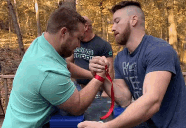 two men arm wrestling with one wearing a shirt that says ' living root ' on it
