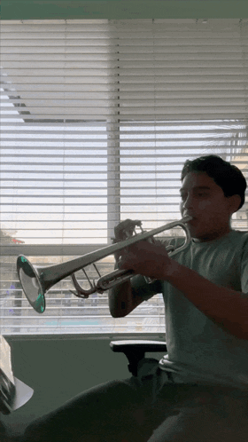 a young man is playing a trumpet in front of a window with blinds