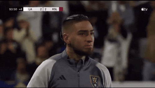 a soccer player stands in front of a scoreboard that says rsl