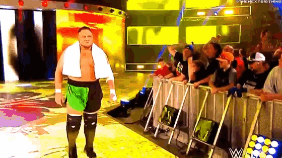 a wrestler with a towel around his neck walks out of a wrestling ring .
