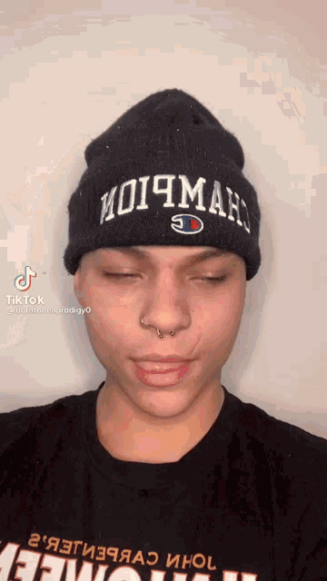 a man wearing a black beanie and a black t-shirt has his eyes closed and his nose ring visible