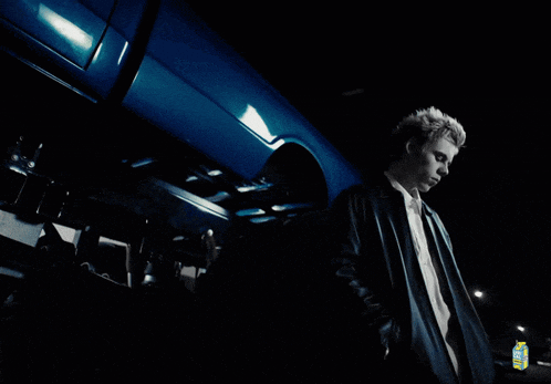 a man is standing next to a blue car with a carton of lemonade in the background