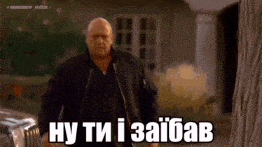 a bald man in a black jacket is standing in front of a car and says `` ну ти і зайвав '' .