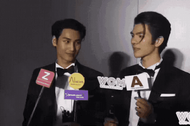 two men in tuxedos are holding signs that say woma