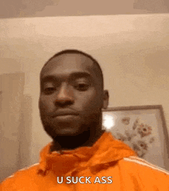 a man in an orange jacket is making a funny face and saying u suck ass .