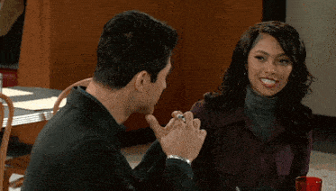a man and woman are sitting at a table with their hands folded