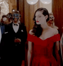 a woman in a red dress is standing in a hallway with people in masks