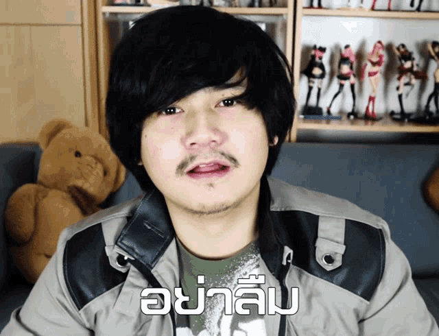 a man sitting on a couch with a teddy bear behind him and a foreign language written on his shirt