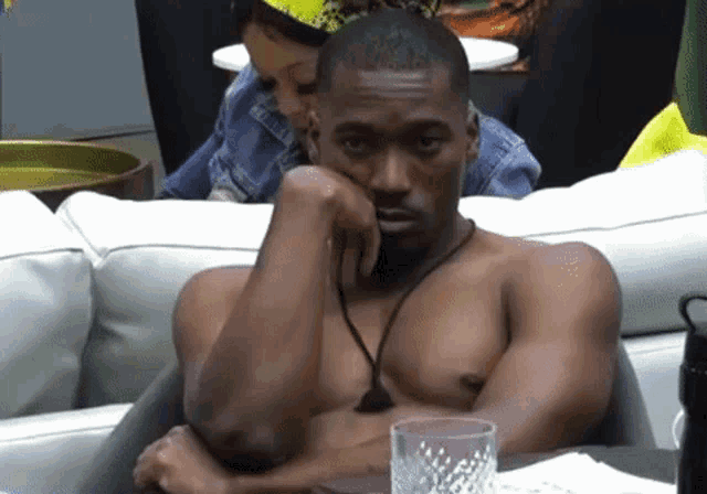 a shirtless man is sitting at a table with a woman behind him