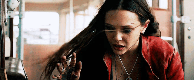 a woman wearing a red jacket and a necklace is looking at her hands .