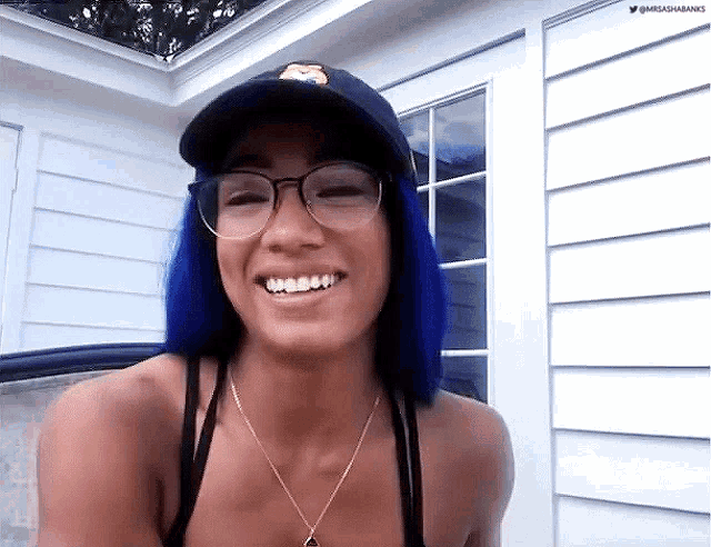 a woman with blue hair is wearing glasses and a hat and smiling