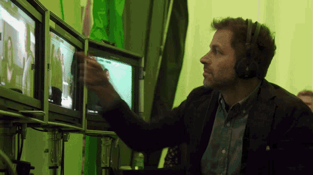 a man wearing headphones looks at a monitor with a green screen behind him