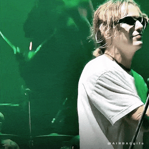 a man wearing sunglasses and a white shirt stands in front of a green background