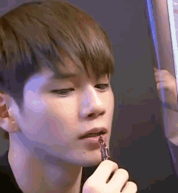a young man is applying lipstick to his lips while looking at himself in a mirror .
