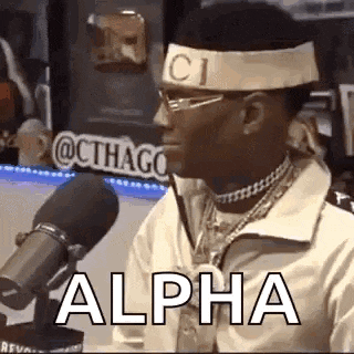 a man wearing a headband and glasses is sitting in front of a microphone and saying alpha .