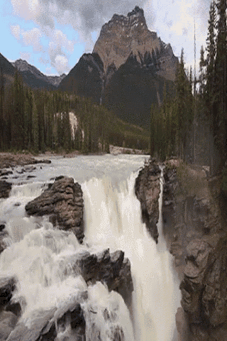 a waterfall surrounded by rocks and trees with a mountain in the background