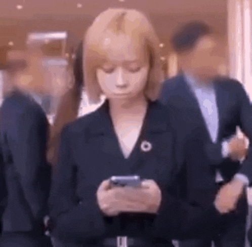 a woman in a suit is looking at her cell phone in a crowd of people .