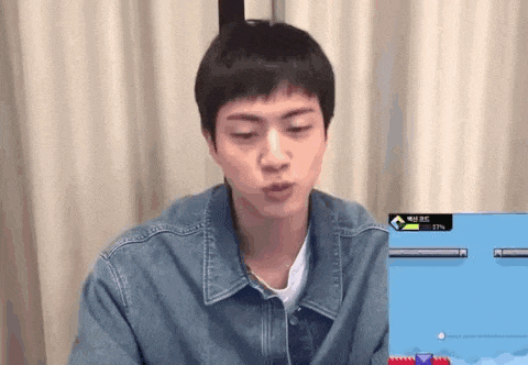 a young man in a denim jacket is sitting in front of a computer screen and making a funny face .