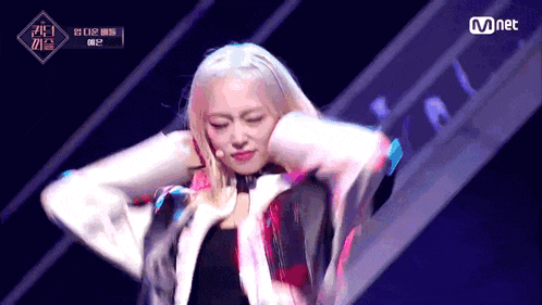 a woman with blonde hair is dancing on a stage with a mnet logo in the corner