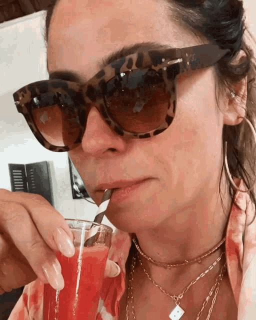 a woman wearing sunglasses is drinking a red drink