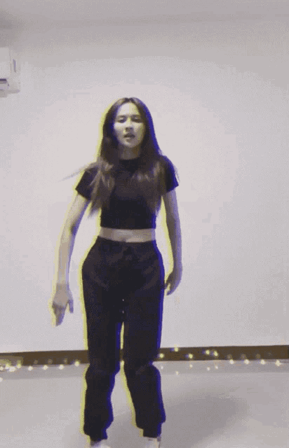 a woman in a black crop top and black pants is dancing in a room