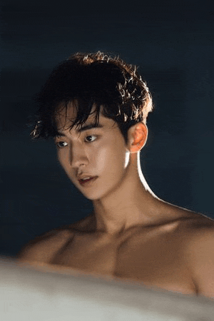 a shirtless young man is standing in a dark room looking at the camera .