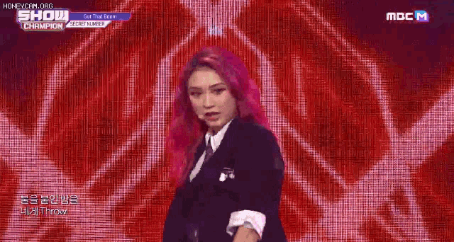 a woman with pink hair is standing on a stage in front of a purple background .