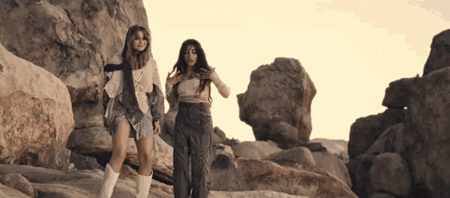 a couple of women standing next to each other on a rocky hillside
