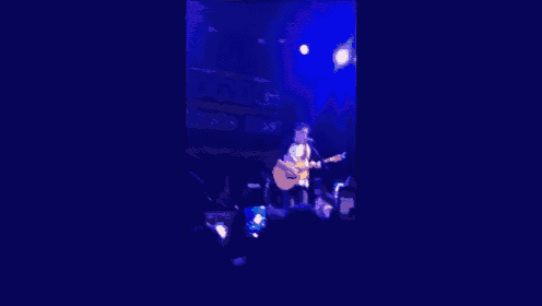 a man is singing into a microphone while playing an acoustic guitar on stage .