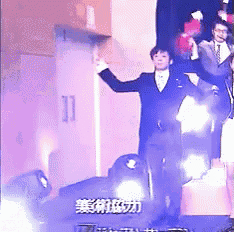 a man in a suit stands on a stage with his arms outstretched in front of chinese writing