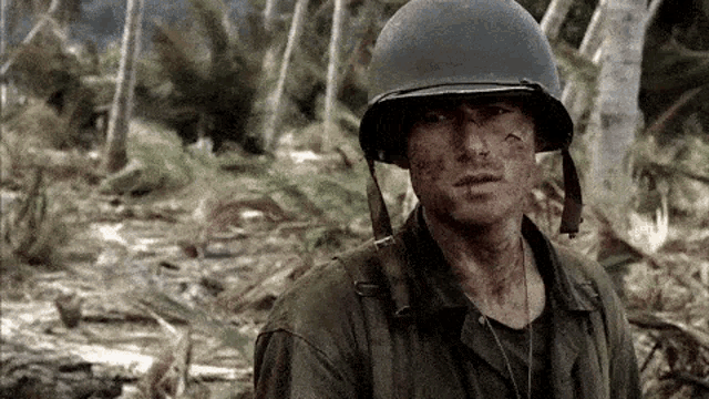 a soldier wearing a helmet is standing in the woods looking at the camera .