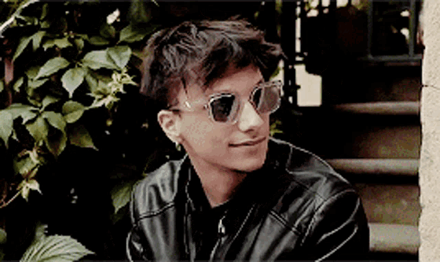 a young man wearing sunglasses and a leather jacket is smiling