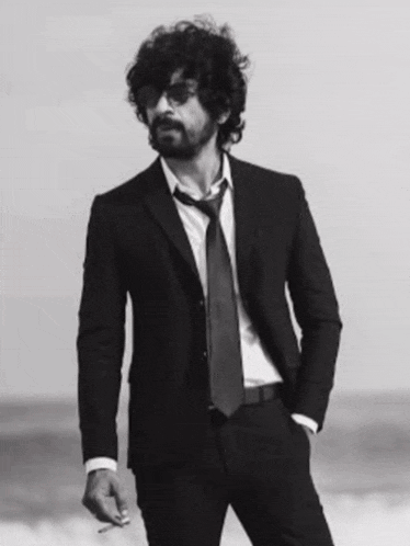 a man in a suit and tie stands on a beach