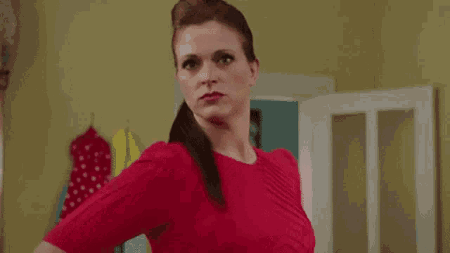 a woman in a red shirt is standing in a room holding a red polka dot dress .
