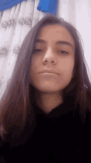 a girl with long dark hair is taking a selfie in front of a blue curtain .