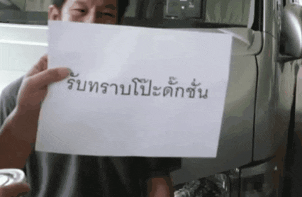 a man is holding a piece of paper with chinese writing on it in front of a truck .