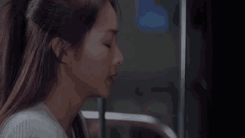a woman is sitting in front of a window with her eyes closed and a ponytail .
