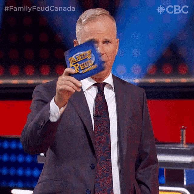 a man in a suit and tie is holding a family feud card in front of his face