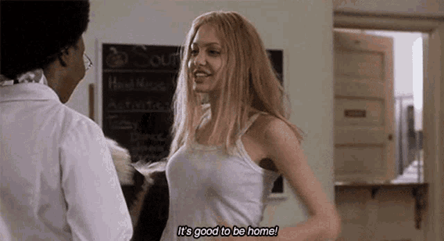 a woman in a white tank top is standing next to another woman in a room and saying it 's good to be home .