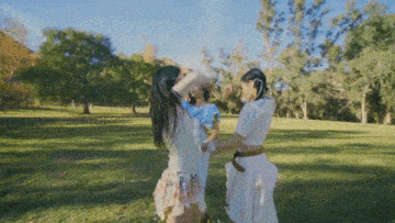 three young women are standing in a park playing with each other