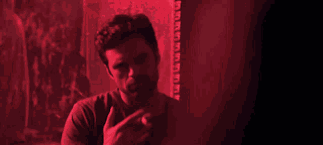 a man is smoking a cigarette in a dark room with a red light behind him
